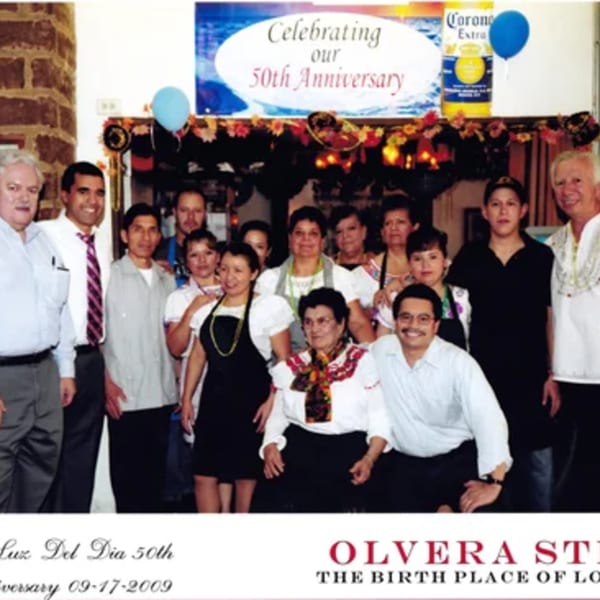 La Luz del Día Restaurant staff and family celebrating their 50th Anniversary under a banner.