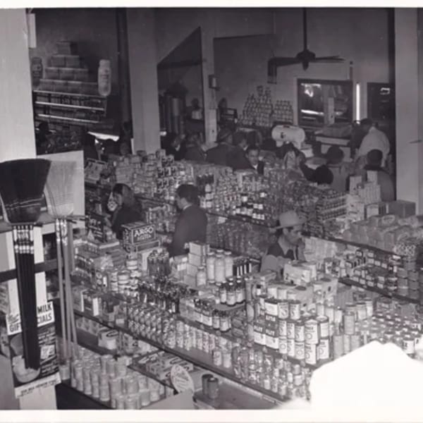 Black and white photo of a busy grocery store with shelves full of products and customers.
