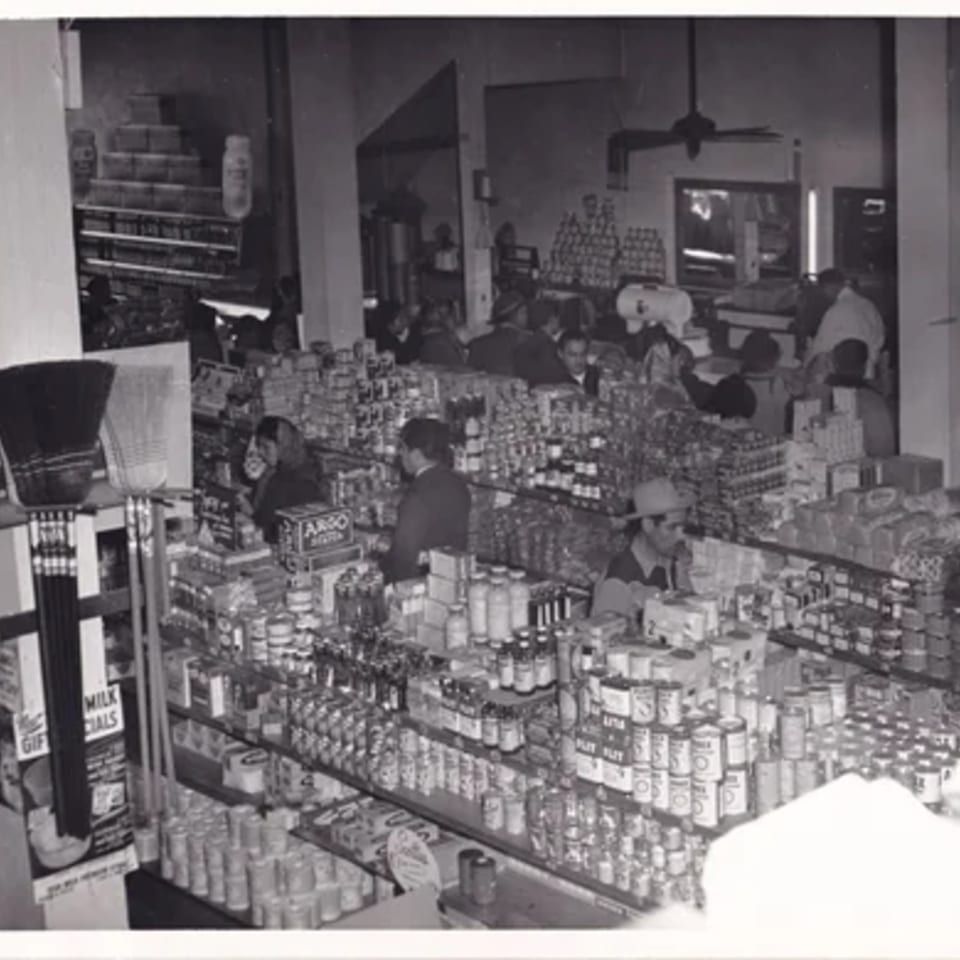 Black and white photo of a busy grocery store with shelves full of products and customers.