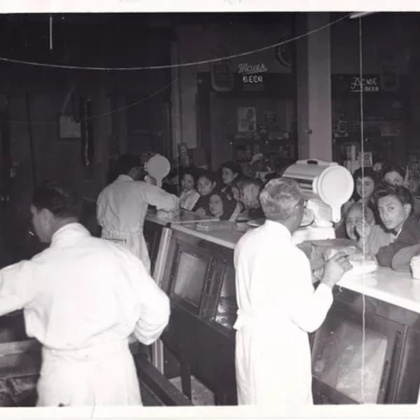 Black and white photo of La Luz del Día Restaurant with cooks serving customers at a counter.
