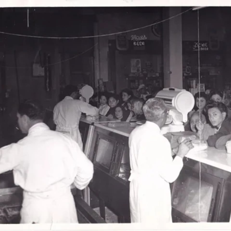 Black and white photo of La Luz del Día Restaurant with cooks serving customers at a counter.