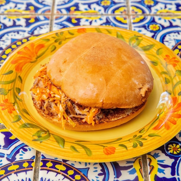 A La Luz del Día Mexican torta with shredded meat and slaw on a yellow floral plate.