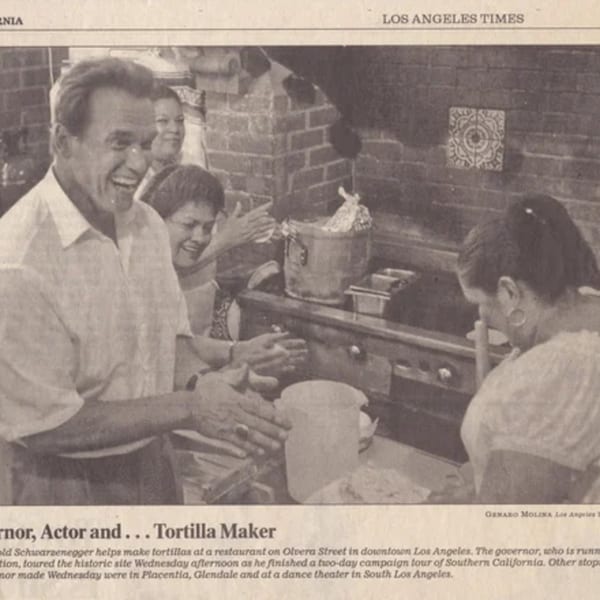 Arnold Schwarzenegger laughing while making tortillas with women at La Luz del Día Restaurant.