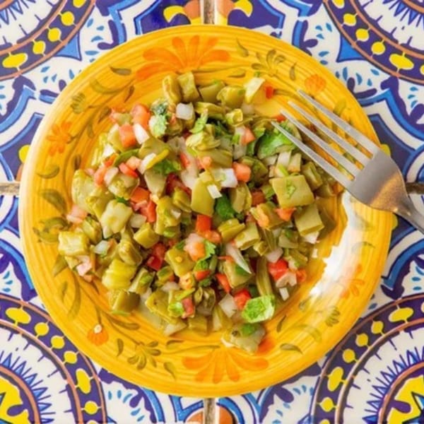 Nopalitos salad with diced tomatoes, onions, and cilantro on a vibrant yellow plate.