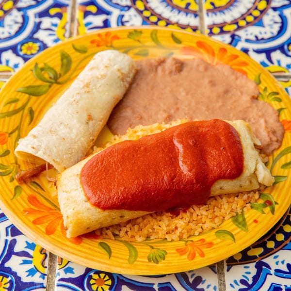 A Mexican combo plate with a tamale, burrito, rice, and refried beans on a yellow plate.