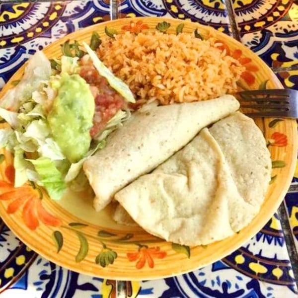 Mexican plate with rice, tortillas, guacamole, salsa, and lettuce on a colorful patterned plate.