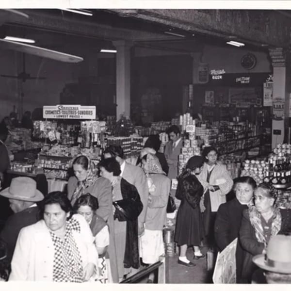 Black and white photo of a busy grocery store with many shoppers and shelves stocked with products.