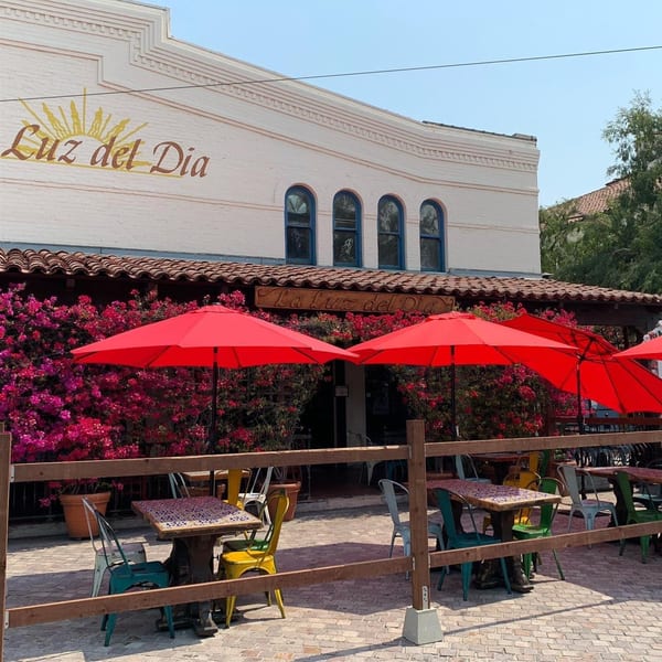 La Luz del Día Restaurant's outdoor patio with red umbrellas, colorful chairs, and blooming bougainvillea.