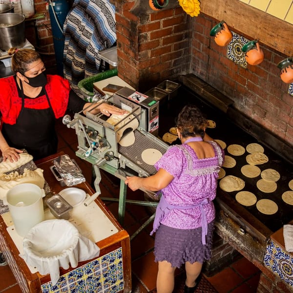 Two women making fresh tortillas using a machine and griddle at La Luz del Día Restaurant.